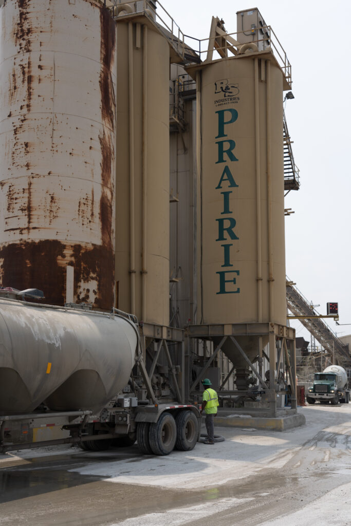 Contact Prairie Materials - weathered cement silos with the Prairie name on the tower above a bulk cement tanker truck